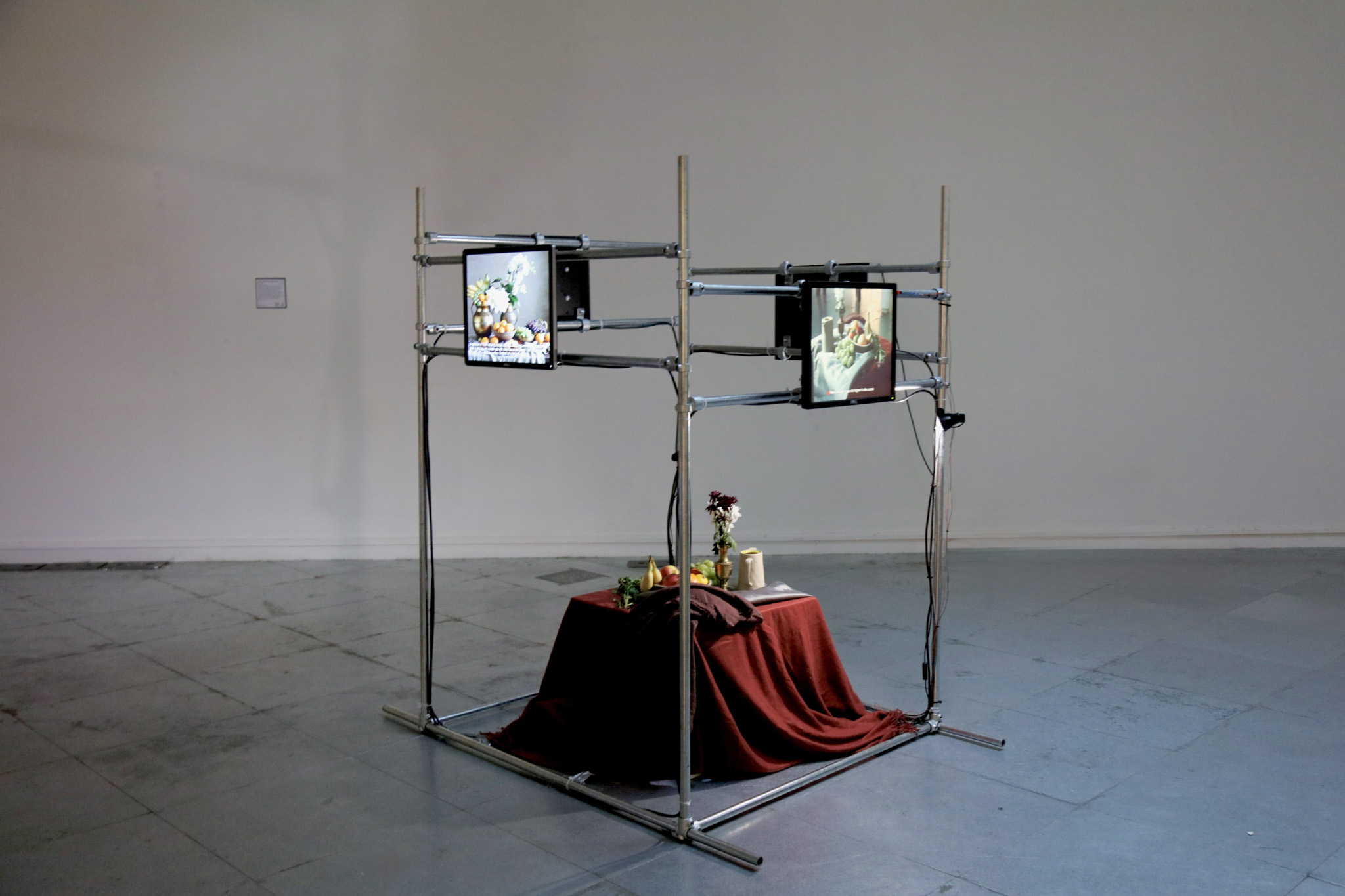 A screen held with metal bars, showing a still life scene of fruit in the centre
